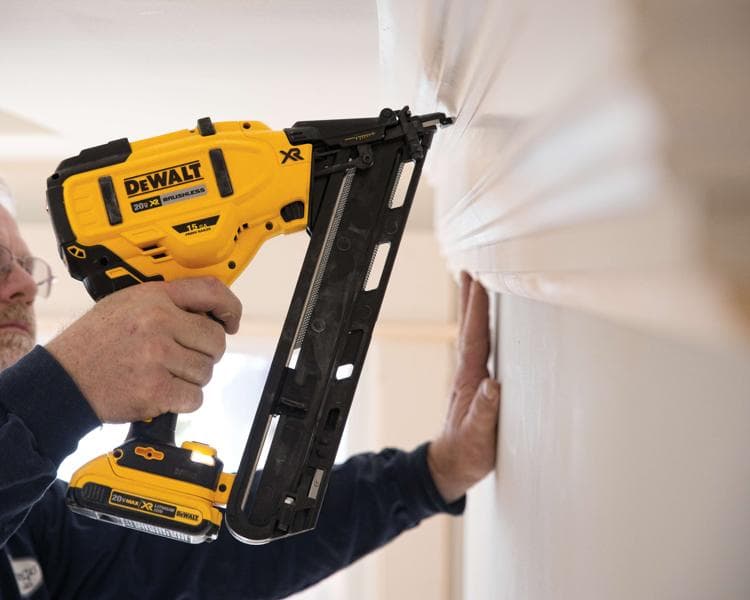 A person using a DEWALT 20V XR cordless brushless nail gun to fasten molding on a wall.